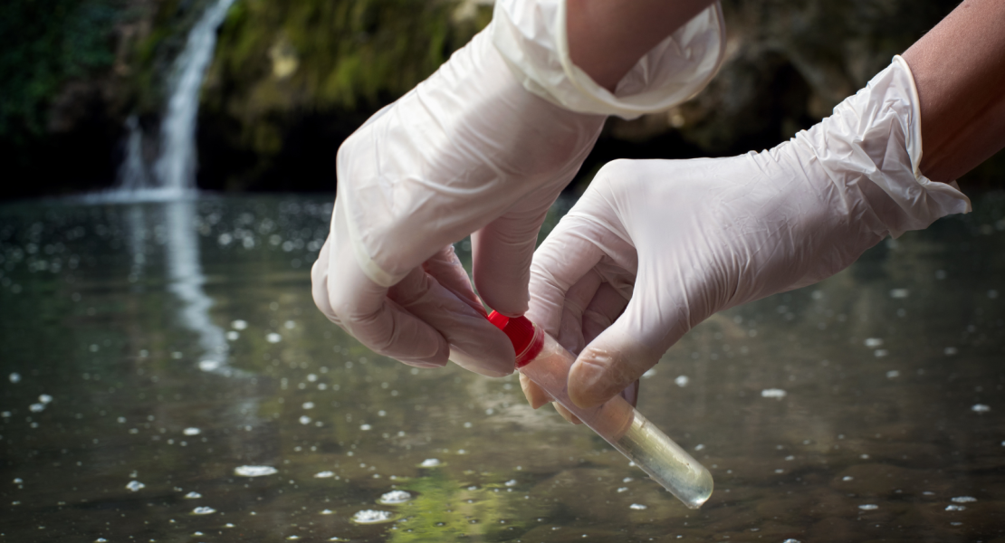 person with gloves on holding test tube near river